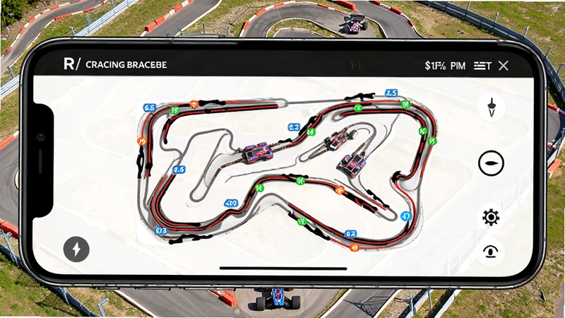 R/CRACING赛道地图管理功能展示,手机屏幕显示带有轨迹标记的赛道平面图,背景为户外遥控车赛道实景航拍,画面清晰明亮