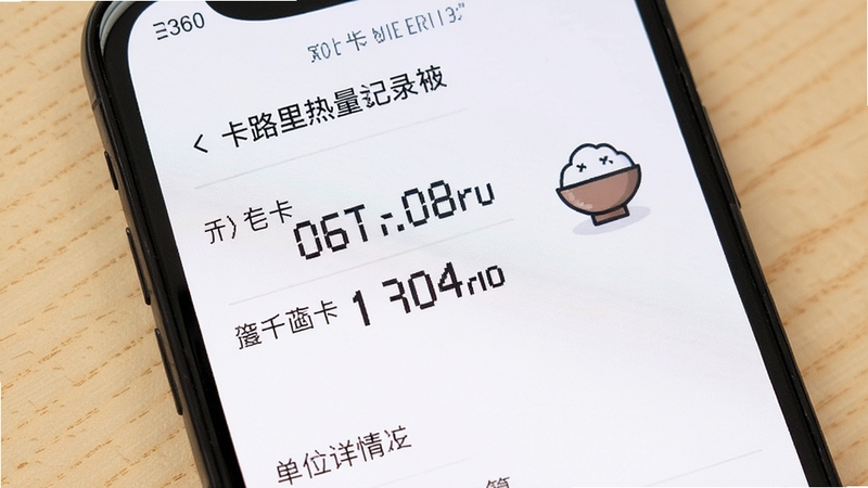 卡路里热量记录本 食物详情页单位换算展示 手机屏幕特写 显示千卡与千焦两个数值 旁边有米饭图标 背景为浅木色 温馨生活风格
