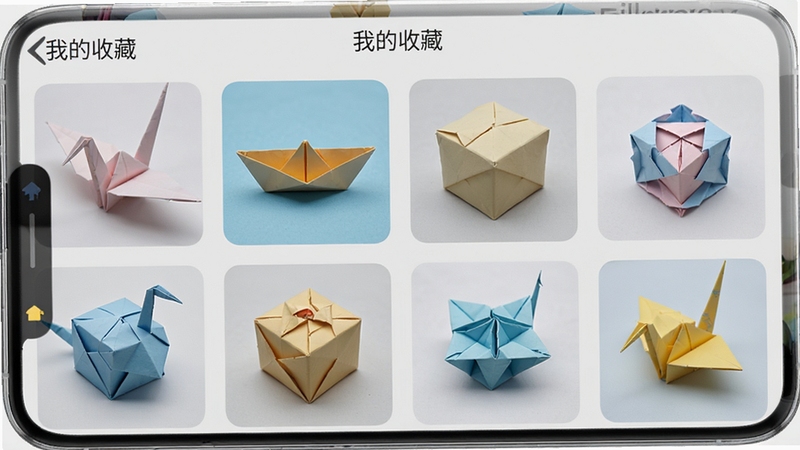 手机屏幕显示折纸应用的收藏夹页面,网格排列着多个折纸作品封面,包括纸鹤、小船、盒子等,页面顶部有“我的收藏”字样,背景是淡灰色,风格简洁现代