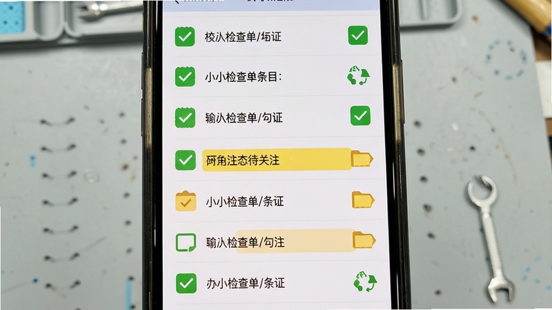 小小检查单条目勾选与状态标记界面,手机屏幕中央展示多条检查项目,部分已勾选为绿色,部分标记为黄色待关注,背景为淡灰色工作台面,整体视觉清晰有序