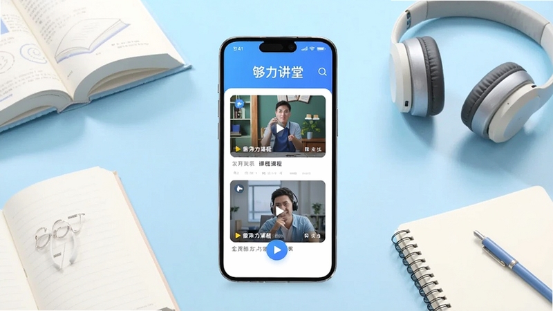 画面中心为一部竖屏智能手机,屏幕上显示够力讲堂应用主界面,包含视频课程卡片与播放按钮,背景为浅蓝色渐变的学习桌面场景,周围点缀书本、耳机与笔记本元素,整体风格清爽明亮,适配Boogu模型生成