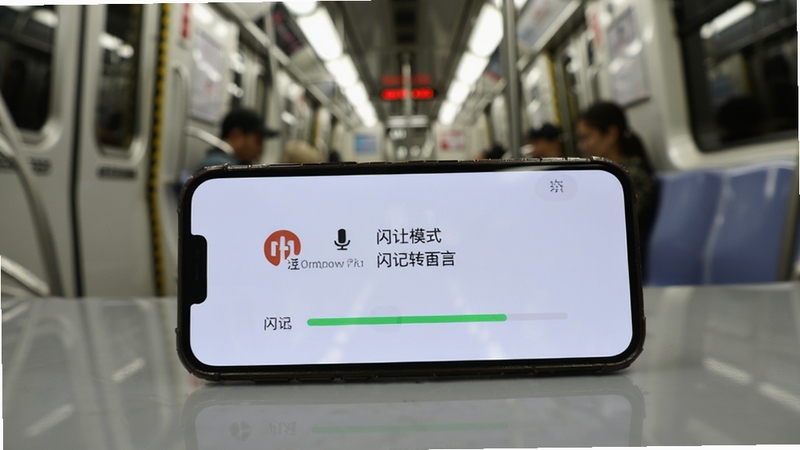 闪记转文字离线转录场景,画面为手机放置在桌面,屏幕显示离线模式标识与转录进度条,背景为地铁车厢内部环境,光线柔和,突出无网络可用特点,画面含闪记转文字名称