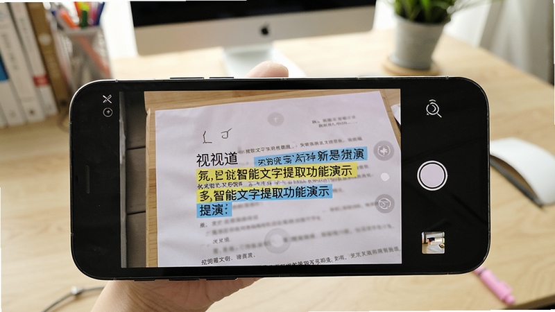 视道 智能文字提取功能演示 手机屏幕显示相机取景框对准文档 识别文字高亮显示 背景为书桌场景 画面清晰明亮 适配Boogu模型生成