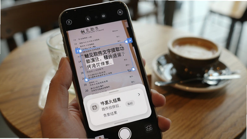触见软件文字提取功能演示,手机屏幕显示拍摄的外文菜单,识别框选中文字段落,下方弹出翻译结果卡片,界面采用浅灰底色与圆角卡片设计,手持手机的自然视角,背景为咖啡厅桌面