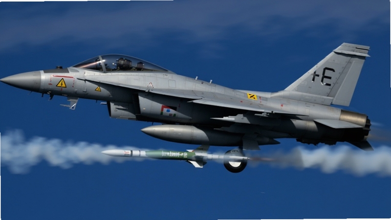 现代喷气战斗机 Modern Jet Fighters Online 导弹发射瞬间特写,一架灰色喷气战机机翼下挂载的导弹拖着白色尾烟离架,背景为深蓝色高空与薄云,画面带轻微动态模糊,机身编号与警示标识清晰可见,写实军事摄影风格