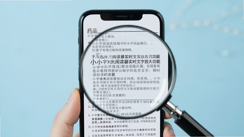 小字放大阅读器实时文字放大功能演示,画面展示手机屏幕中一份药品说明书的小字被放大后清晰可读,放大镜效果突出,背景为柔和的浅蓝色,整体视觉简洁直观
