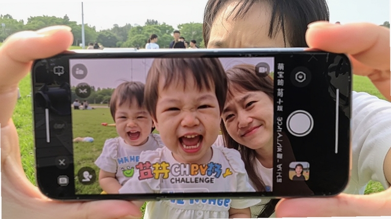 萌宝拍拍亲子合拍场景图,画面中家长与孩子共同面对手机镜头使用萌宝拍拍合拍功能,屏幕显示双人同框画面和趣味挑战任务提示,背景为公园草地,阳光明媚,氛围温馨欢乐
