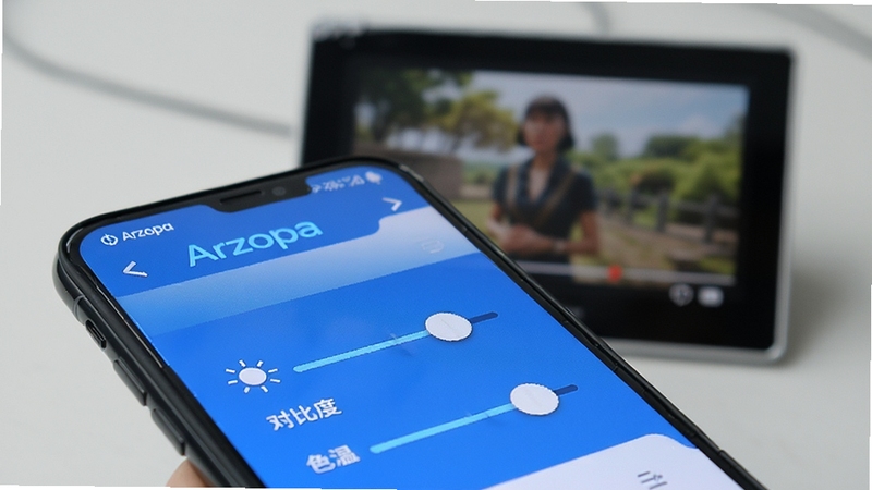 Arzopa应用内显示参数调节界面特写,手机屏幕上呈现亮度、对比度、色温滑块控件,背景虚化展示一台正在播放视频的Arzopa便携屏,界面设计清爽现代,蓝白配色,科技感十足