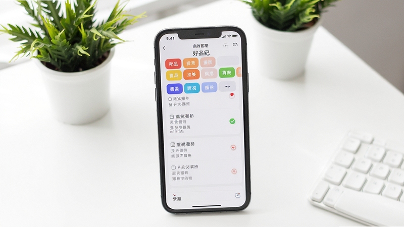 好品纪应用内的清单分类管理界面,手机屏幕显示多个彩色分类标签和整齐的条目列表,背景是干净的白色桌面和绿植,画面明亮清爽,体现高效整理的氛围