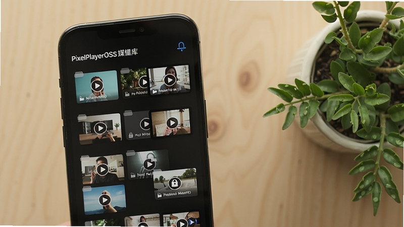 PixelPlayerOSS媒体库列表界面,手机屏幕展示按文件夹分类的视频缩略图网格,其中一个文件夹带有锁形隐藏标识,背景为浅色木质桌面与绿植,风格清新自然,强调本地管理与隐私安全