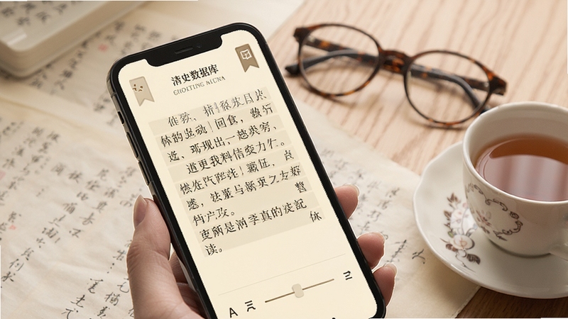 展示手机屏幕中清史数据库的阅读界面,文字排版疏朗,背景为米黄色护眼底色,页面边缘有书签图标与字号调节滑块,旁边放置一副眼镜与一杯茶,营造舒适阅读场景