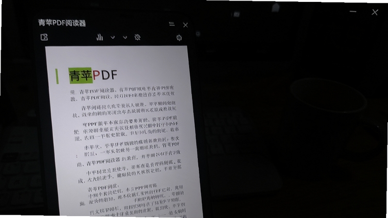 青苹PDF阅读器夜间模式效果,屏幕上PDF页面呈现深色背景,文字清晰,周围环境昏暗,手机或电脑屏幕光线柔和,软件名称“青苹PDF阅读器”在屏幕左上角显示