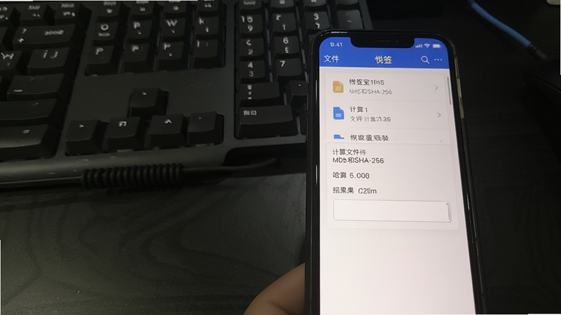 悦签宝文件校验功能截图,手机屏幕显示悦签宝计算文件的MD5和SHA-256值,界面有文件列表和哈希结果输出框,背景为深色桌面,电脑键盘与手机同时入镜,体现工具在文件管理中的实用性。