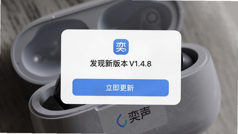 奕声app的固件升级页面,手机界面中显示“发现新版本V1.4.8”的弹窗,下方有“立即更新”按钮,背景是耳机充电盒的微距照片,光线柔和,突出软件更新功能的专业与可靠,画面中融入“奕声”的品牌标识。