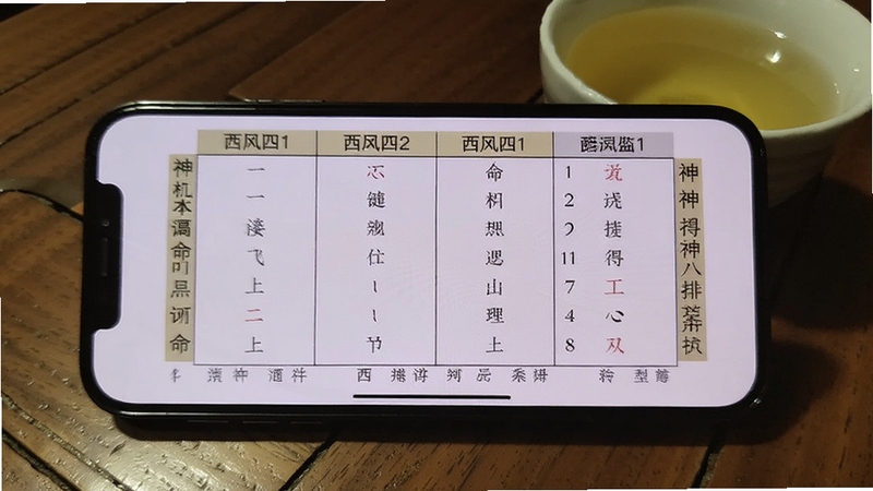 手机屏幕显示西风四柱八字排盘系统导出的命盘图片,画面中手机横屏放置,屏幕内容清晰展示四柱表格与神煞标注,背景为木质桌面和一杯清茶,整体氛围安静适合研究命理