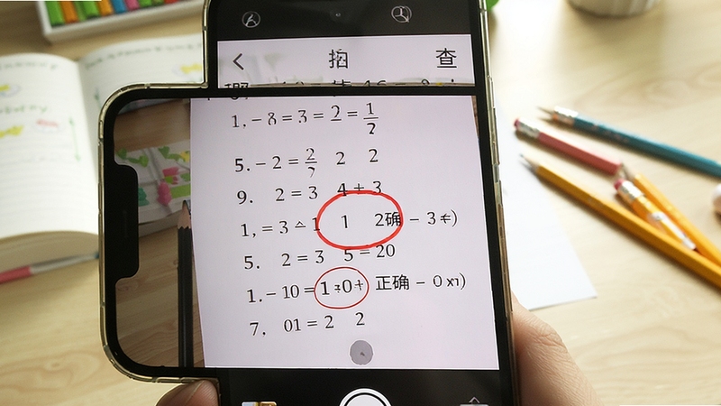拍照查 作业检查界面 手机拍摄一页数学口算题 屏幕上用红色圆圈标出错误答案 旁边显示正确答案 背景是书桌和铅笔 光线明亮