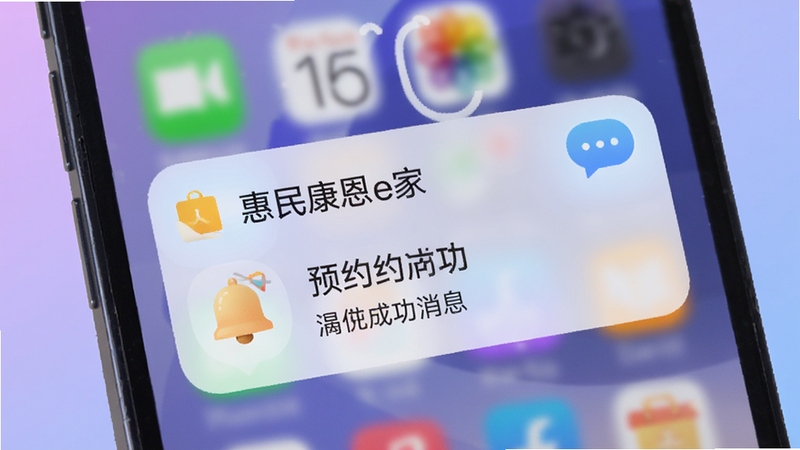 手机锁屏界面弹出惠民康恩e家的通知提醒,显示预约成功消息,背景是柔和的紫蓝色渐变,画面中有铃铛图标和消息气泡元素,风格现代简洁,突出即时提醒功能