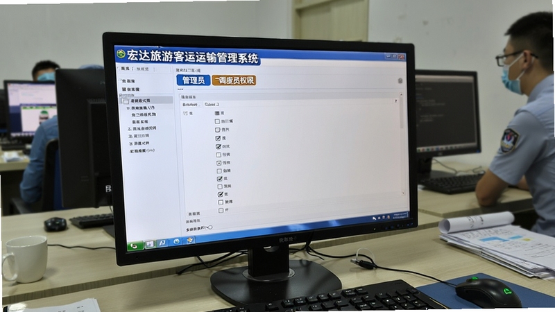 宏达旅游客运运输管理系统 多用户权限设置界面,画面主体为电脑屏幕显示角色权限勾选列表,背景为IT管理员工作台,屏幕上有管理员与调度员权限标签