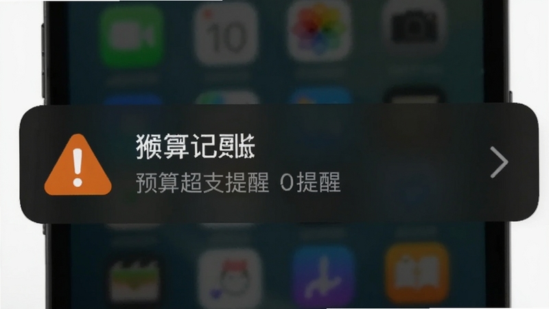 猴哥记账预算提醒弹窗示意图,画面中手机锁屏界面显示一条预算超支提醒通知,背景为深色模式,通知卡片上有醒目的橙色警示图标
